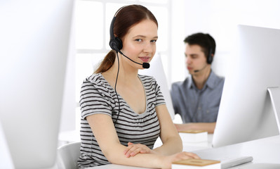 Group of operators at work. Call center. Focus on beautiful woman receptionist in headset at customer service. Business concept and casual striped clothing style