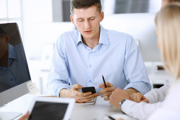 Group of business people discussing questions at meeting. Headshot of casual dressed businessman using smartphone at office negotiation. Teamwork and cooperation in corporate occupation