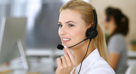 Blonde business woman using headset for communication and consulting people at customer service...