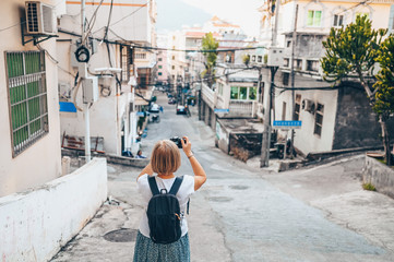 Elderly senior Asian traveling backpacker mature woman tourist walking enjoying taking photos in Sanya local street outdoor. Traveling along Asia, active lifestyle concept. Discovering Hainan, China