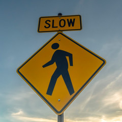 Square frame Yellow Slow sign and pedestrian crossing sign against cloudy sky at sunset