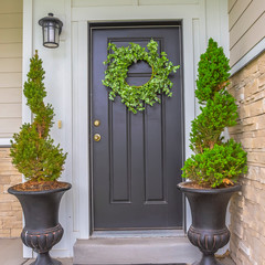 Square Gray front door of a home with green wreath and flanked by tall potted plants