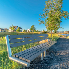 Obraz premium Square Bench at the shore of a lake with homes and buildings background on a sunny day