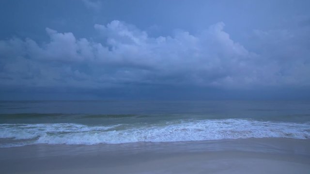 Multiple lightening strikes illuminates the soft white sky as a storm brews on the horizon of the ocean on the Gulf of Mexico near dark making the teal and blue waves even more ethereal. 