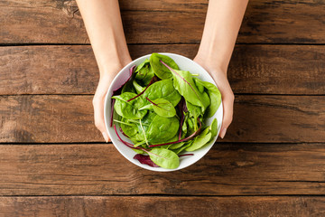 Female hands holding green salad in bowl on rustic wooden background. Top view. Close up