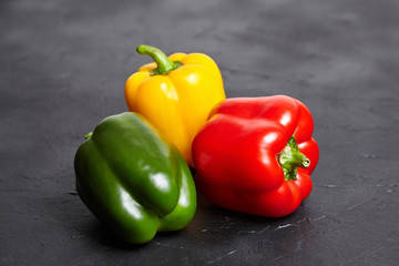 Red, green, and yellow bell peppers on  black background. Three sweet peppers in different colors on stone table, vegetable ingredient, healthy food