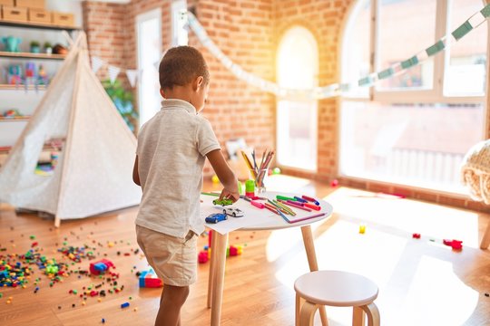 Beautiful african american toddler playing with cars around lots of toys at kindergarten