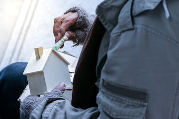 a old man is homeless or beggar sitting or sleeping beside street with cup for request some coin...