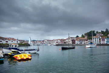 Fototapeta na wymiar Boats moored in the fishing port of Saint-Jean-de-Luz / Ciboure (France). French Basque country. Coastal town on the shore of the Bay of Biscay in cloudy weather day with grey sky