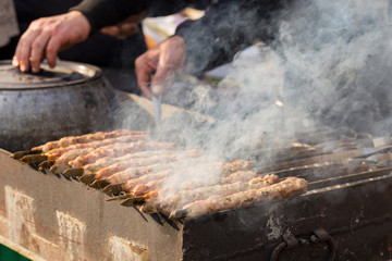 Meat slices prepare on fire. Baked meat on skewers. A cook is preparing a hot meal outdoors. Hands of the master.