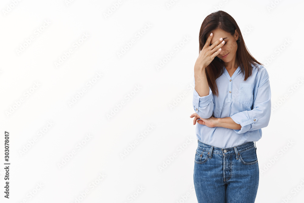 Wall mural Embarrassed annoyed adult woman hiding face bend head down, facepalm, smirk irritated, not looking friend acting weird, feel humiliated uncomfortable, standing white background