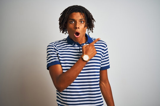 Afro man with dreadlocks wearing striped blue polo standing over isolated white background Surprised pointing with finger to the side, open mouth amazed expression.