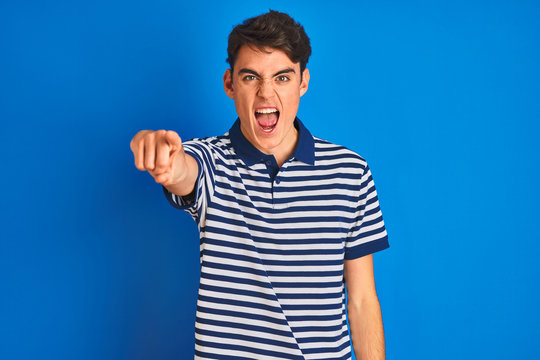 Teenager boy wearing casual t-shirt standing over blue isolated background pointing displeased and frustrated to the camera, angry and furious with you