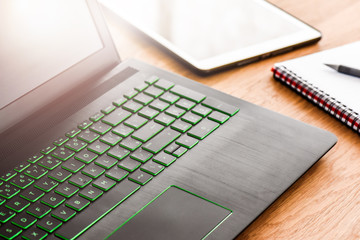 Desk laptop or modern computer with blank screen on rustic table. Spiral notepad placed on wooden desktop with pen and backlight. Business notebook detail concept.