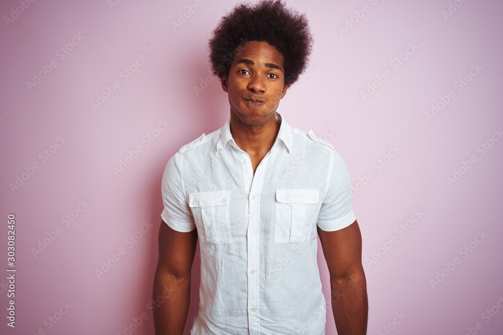 Poster Young american man with afro hair wearing white shirt standing over isolated pink background puffing cheeks with funny face. Mouth inflated with air, crazy expression.