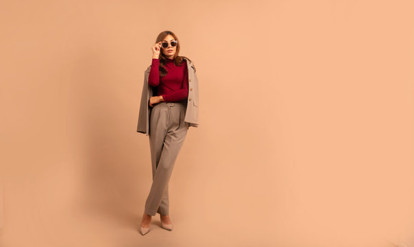 Full length studio portrait of young business woman. Full length portrait of smiling attractive businesswoman in suit posing while standing with arms crossed and looking at camera isolated over beige