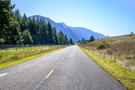 Empty road along the river bank with mountains and trees in Columbia Gorge