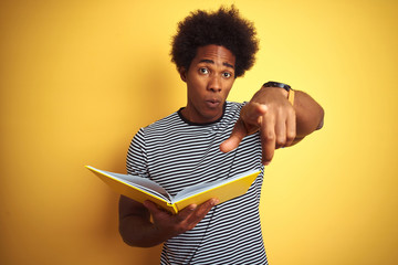 Afro american student man reading book standing over isolated yellow background pointing with...