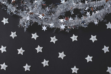 Tinsel and stars on a dark background. Shiny stars of silver color. New Year concept. Simple flat lay composition