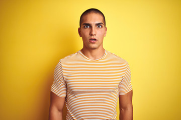 Young handsome man wearing striped t-shirt over yellow isolated background afraid and shocked with surprise expression, fear and excited face.