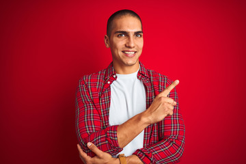 Young handsome man wearing a shirt using watch over red isolated background with a big smile on face, pointing with hand and finger to the side looking at the camera.