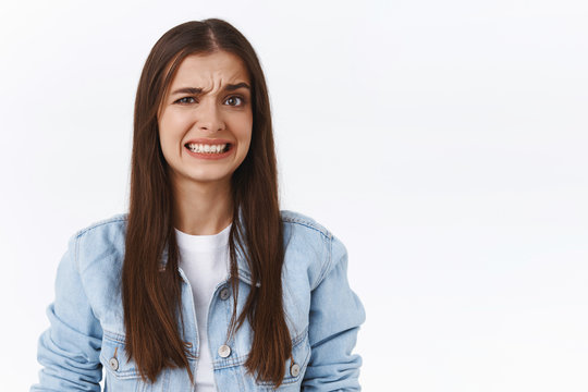 Girl cringe as seeing something embarrassing and bothering. Woman make uncomfortable smile and squinting feeling worried and displeased, see bothering bad situation, standing white background