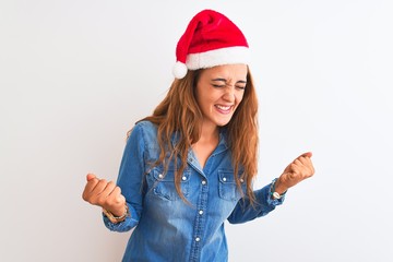 Obraz na płótnie Canvas Young beautiful redhead woman wearing christmas hat over isolated background very happy and excited doing winner gesture with arms raised, smiling and screaming for success. Celebration concept.