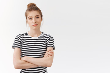 Self-assured confident young skeptical woman with messy bun in striped t-shirt, cross hands chest...