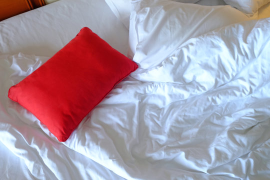 Red pillow on white and clean unmade bed