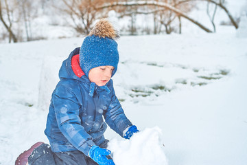 Fototapeta na wymiar little boy in a hat and mittens makes a snowman in winter