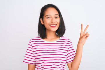 Young chinese woman wearing striped t-shirt standing over isolated white background showing and pointing up with fingers number two while smiling confident and happy.