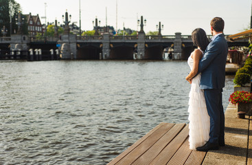 Groom embracing his bride from behind, looking out at the water on an Amsterdam canal
