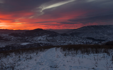 Winter sunset snow field on top of mountain slope on the background of  hills under colorful sky