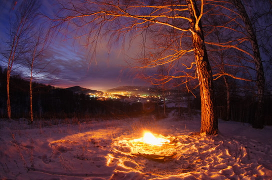 Night fire on the mountain on the background of the bright sunset town village under a dark sky