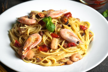 Pasta with seafood, sun-dried tomatoes, parmesan and basil on a light plate on a dark background top view copy space.