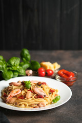 Pasta with seafood, sun-dried tomatoes, parmesan and basil on a light plate on a dark background top view copy space.