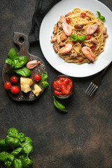Pasta with seafood, sun-dried tomatoes, parmesan and basil on a light plate on a dark background top view copy space.