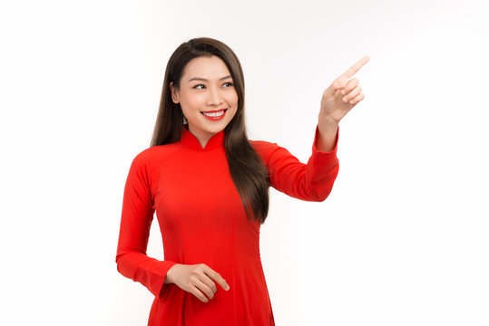 Portrait of young Asian woman wearing a red ao dai and showing hand to somewhere on white background.