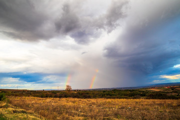 Fototapeta na wymiar Rainbow in a dark clouds above the meadow