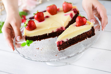 Woman serving finest tart on glass tray or dish. Delicious cake with strawberry on top in beautiful hands.