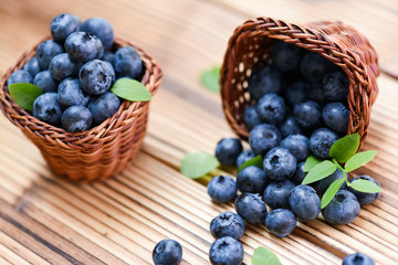 Blueberries in wicker basket on old wooden table. Blueberry with green leaves.