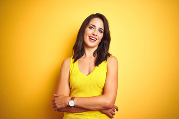 Young beautiful woman wearing t-shirt standing over yellow isolated background happy face smiling with crossed arms looking at the camera. Positive person.