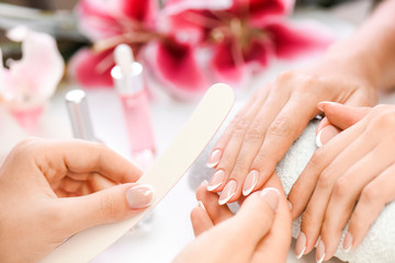 Obraz na płótnie Canvas Woman beautician using a nail file. Professional and beautiful hands with nails care manicure applying in luxury salon. Pink red flowers background.