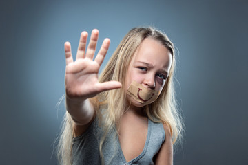 Sad and frightened little girl with bloodshot, bruised eyes and false smile on her mouth. Concept of child violence, domestic abuse. Depressed being victim of parents. Illusion of happy childhood.