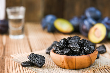 Prunes in wooden bowl on rustic table. Plums and brandy or slivovitz in small glass background.