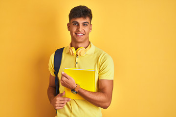 Indian student man wearing backpack headphones notebook over isolated yellow background with a happy face standing and smiling with a confident smile showing teeth