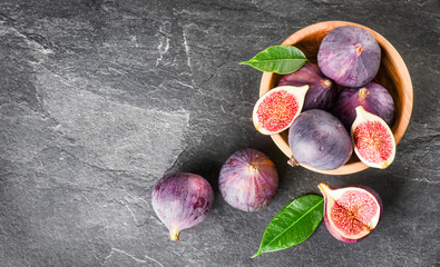 Fresh figs in round wooden bowl on dark stone table, space for text. Ripe fig fruits with leaves on...
