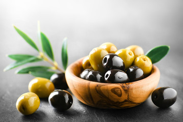 Fresh olives with core in olive bowl on dark stone table and green leaves.
