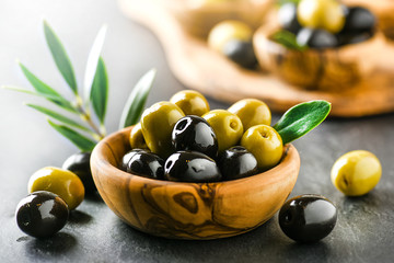 Verse olijven met kern in olijfkom op donkere stenen tafel en groene bladeren.