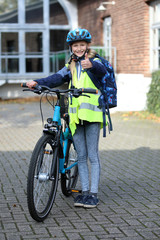 Schulkind mit Fahrrad, trägt Helm und Warnweste und zeigt Daumen hoch 